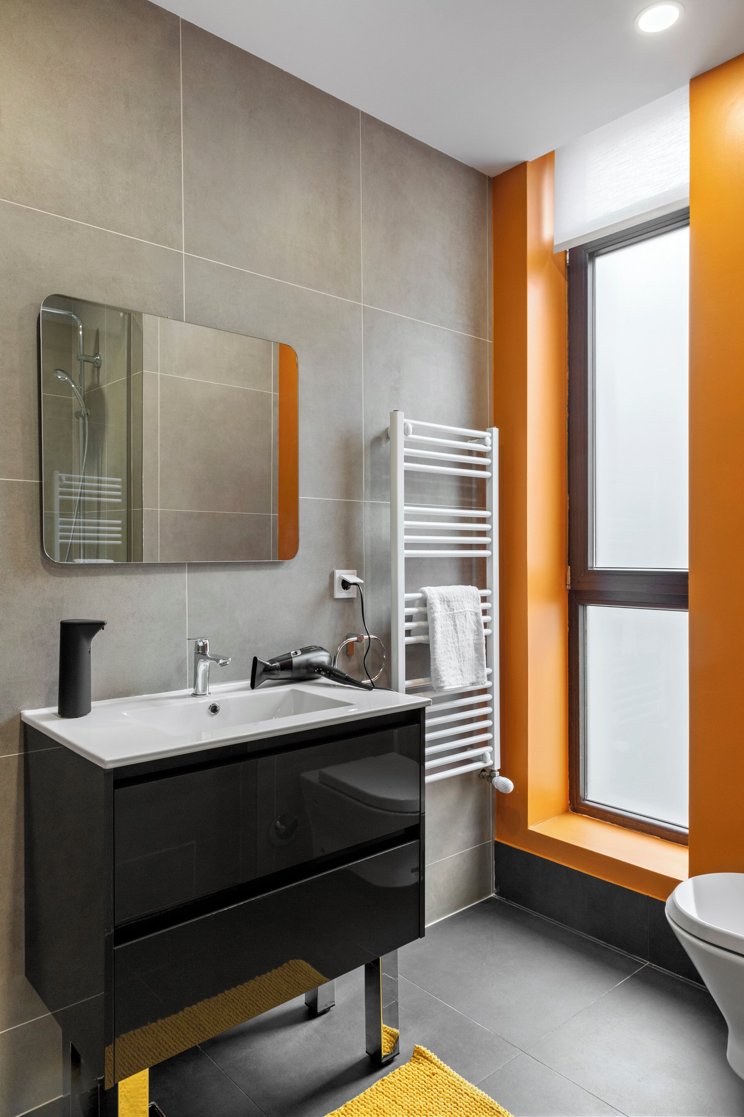 Un baño moderno con un espejo grande, un lavamanos blanco, un perchero y una ventana.