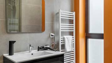 A modern bathroom with a large mirror, a white sink, a towel rack, and a window.