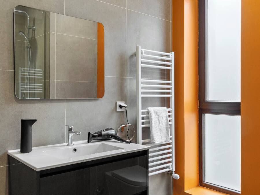 A modern bathroom with a large mirror, a white sink, a towel rack, and a window.