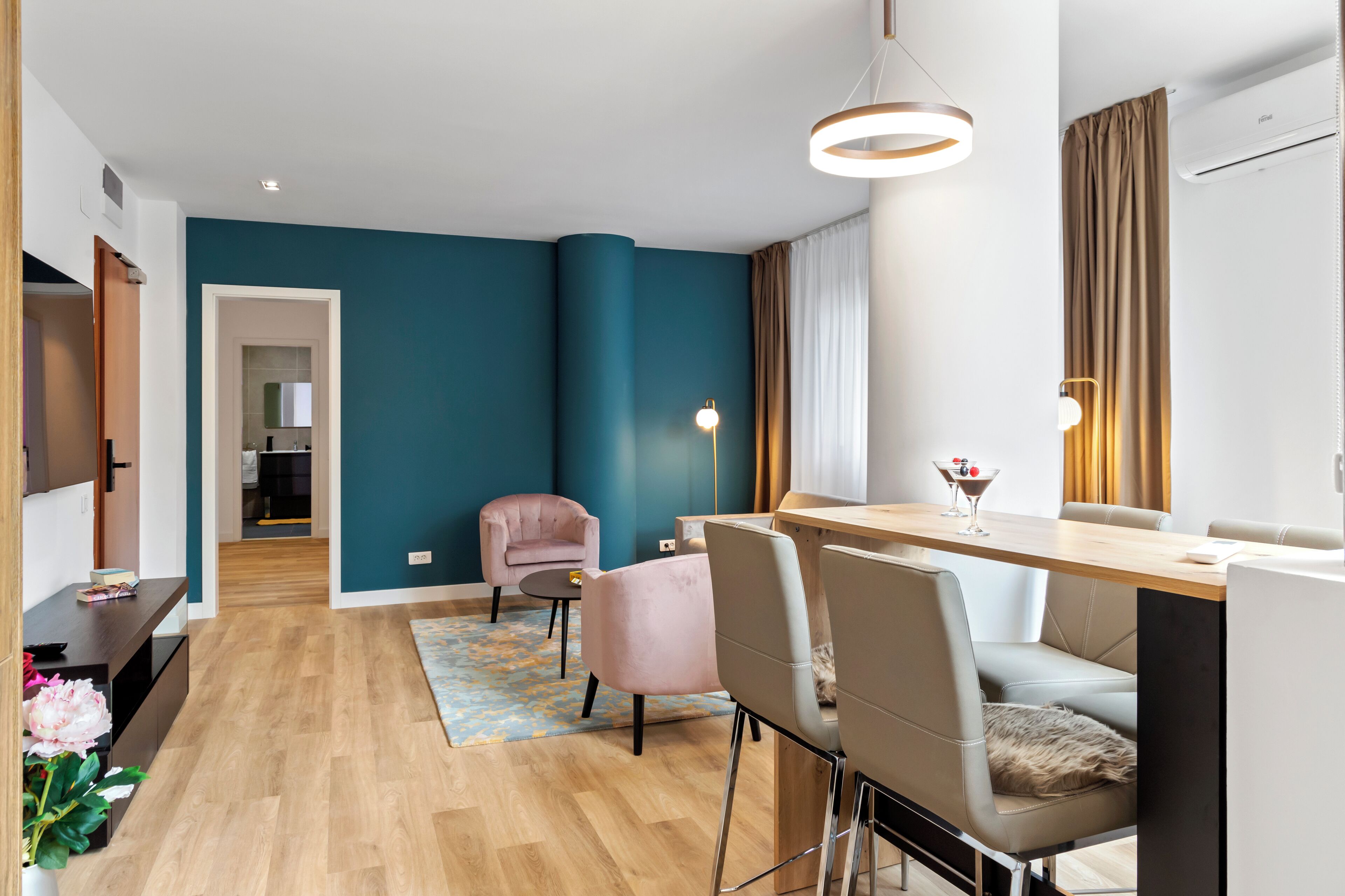 A modern living room with teal walls, a wooden floor, and a dining area with a table and chairs.