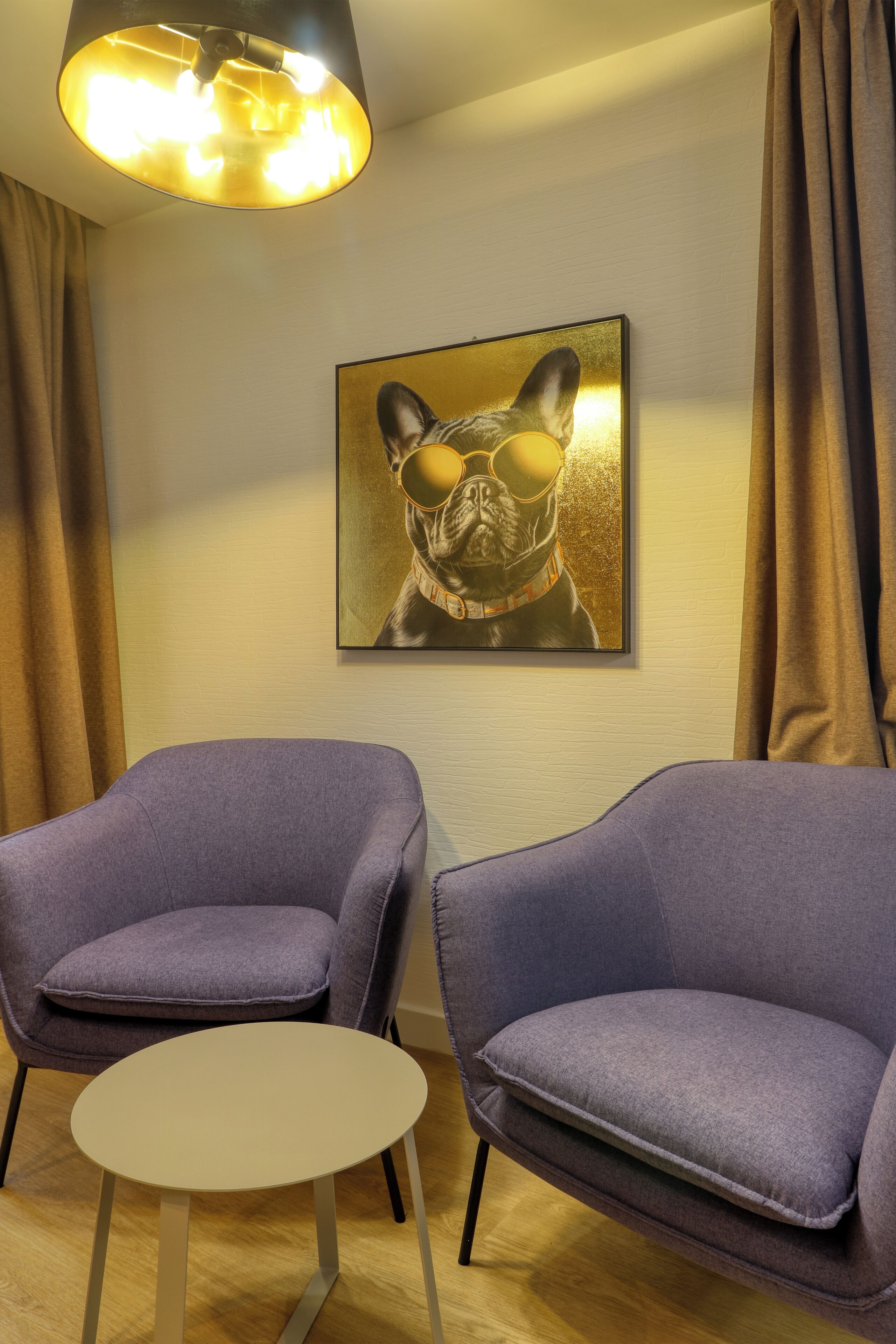 A room with two purple armchairs, a small round table, and a framed picture of a dog on the wall.