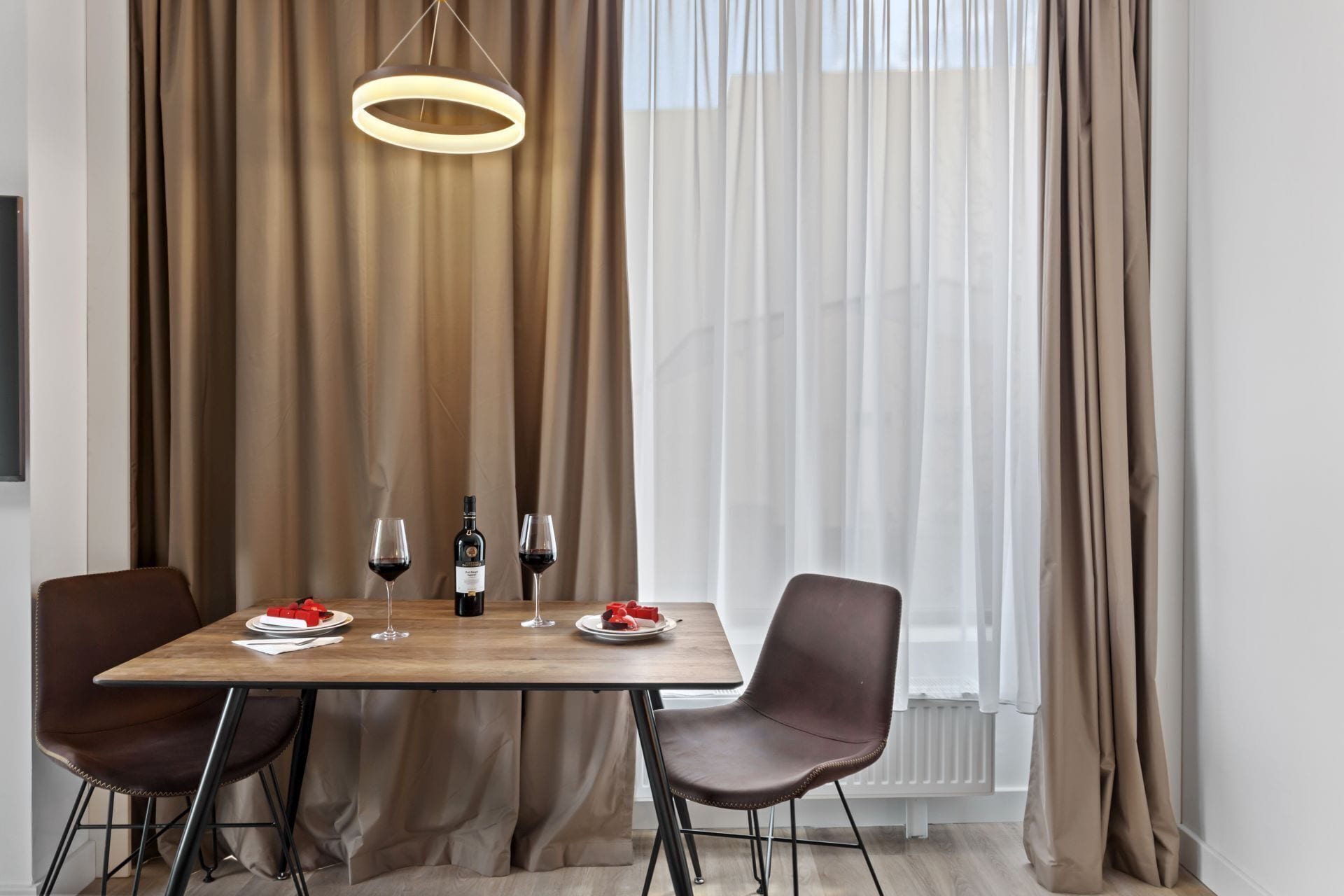 A dining area with a table set for two, two wine glasses, a bottle of wine, and a plate of food.