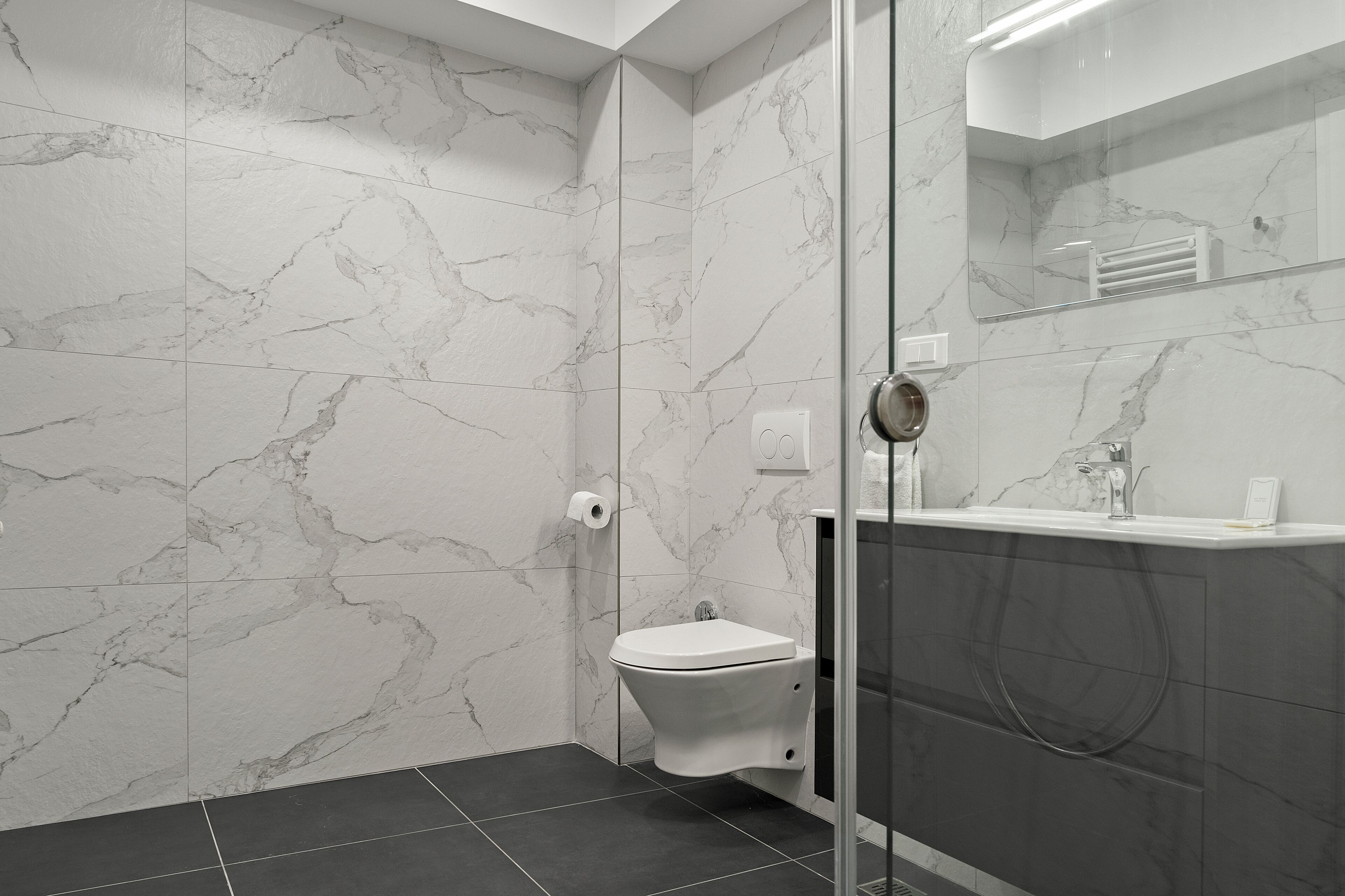 Un baño moderno con inodoro, cabina de ducha de vidrio y pared de mármol.