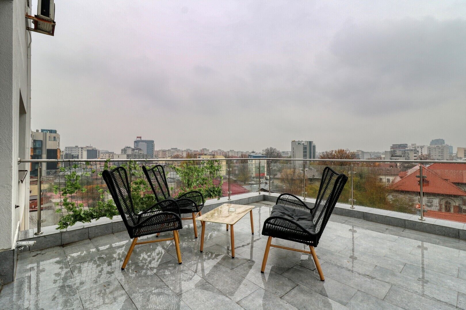 Un balcón con dos sillas negras y una mesita pequeña, con vistas a un paisaje urbano.