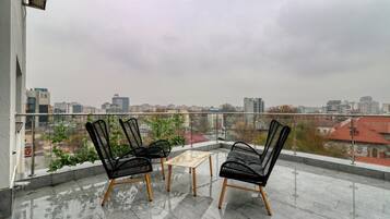 Un balcón con dos sillas negras y una mesita pequeña, con vistas a un paisaje urbano.