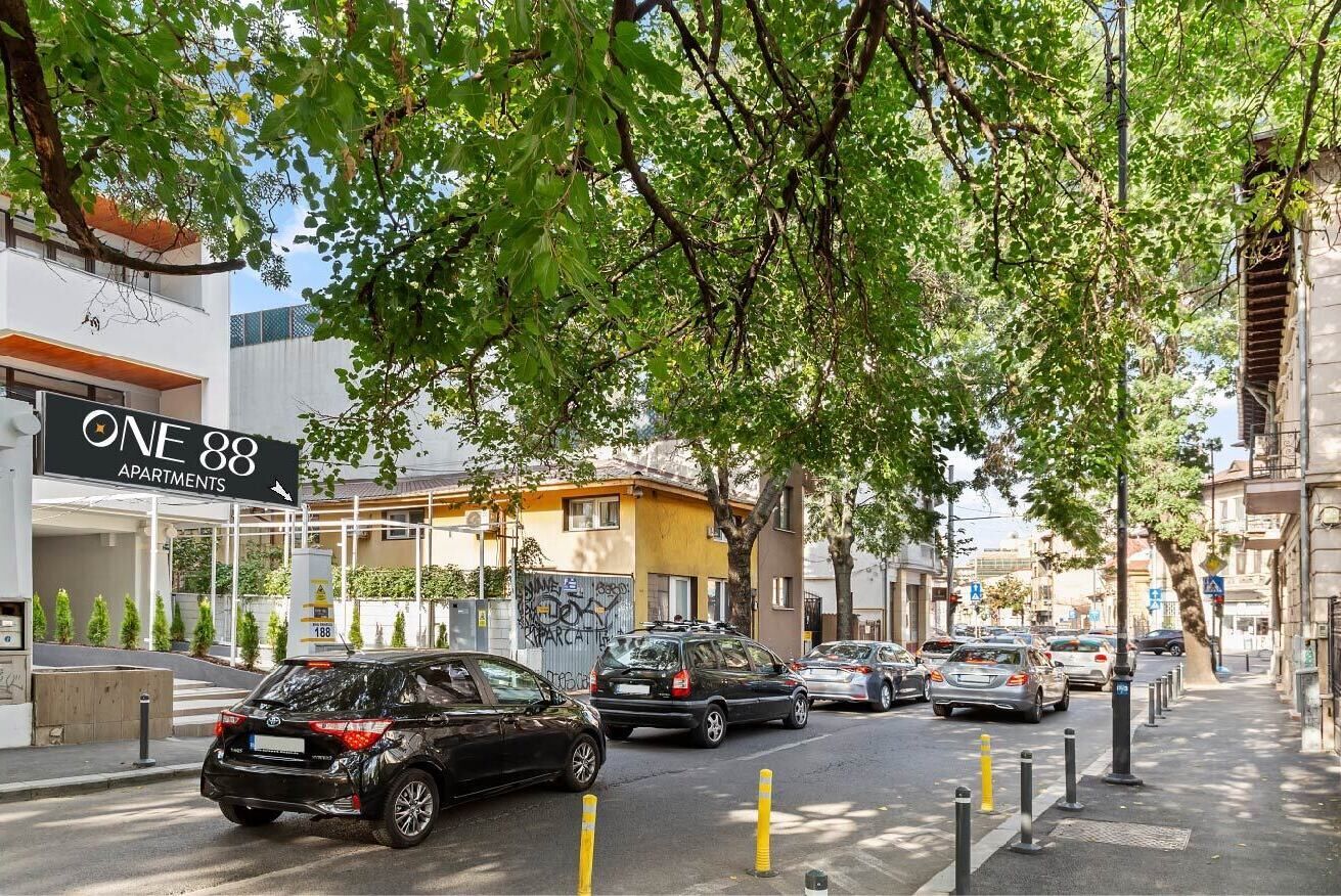 A street view with parked cars, a building labeled "ONE 88 APARTMENTS," and trees lining the sidewalk.