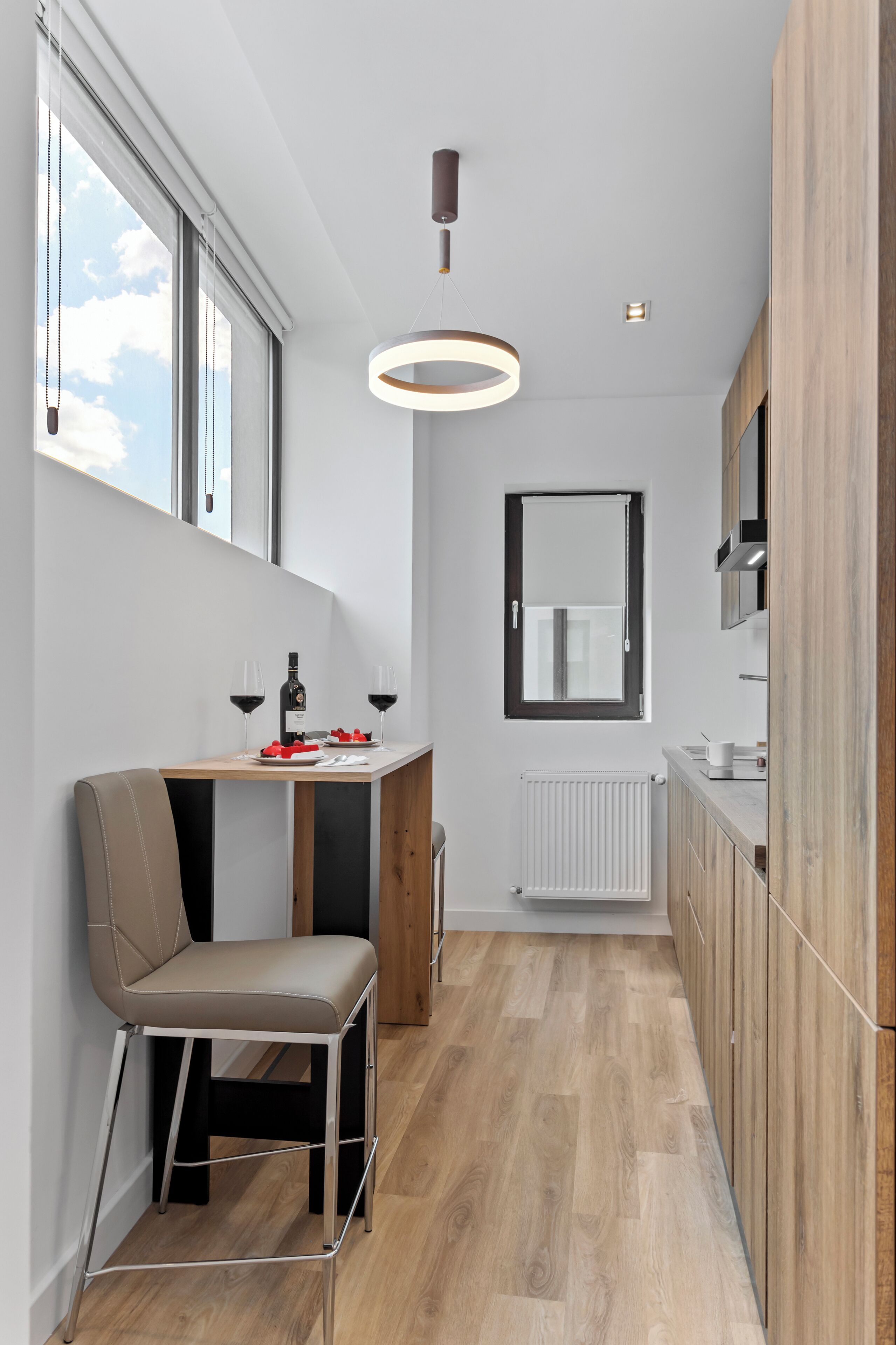 A modern kitchen with a dining area, wooden cabinets, a window, and a pendant light.