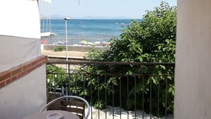 A balcony with a table and chairs, overlooking a beach with people and boats. - Hotel Sibilla Residence (Pozzuoli)