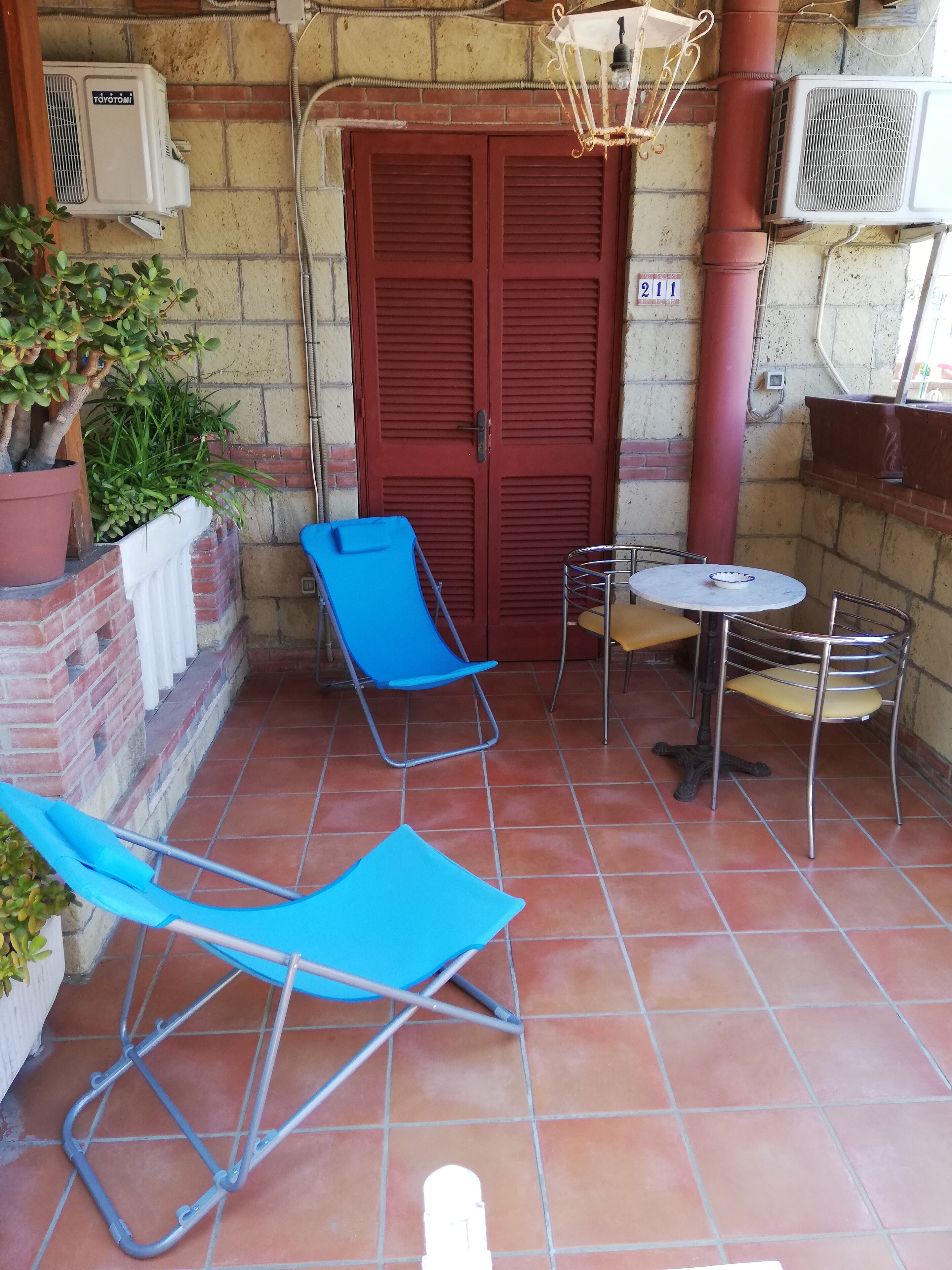 A patio with two blue chairs, a small round table, and a red door.