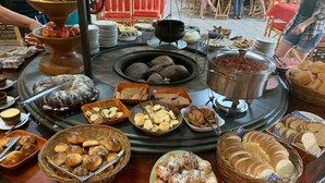Una mesa de buffet con diversas opciones de comida, incluyendo pan, bollería y frutas.