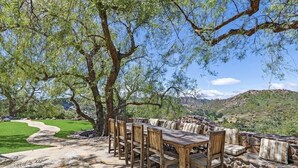 Zona pranzo all'aperto con parete in pietra, mobili in legno e vista su un campo da golf e delle colline.