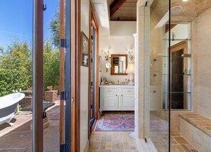 Une salle de bain avec une douche à parois de verre, un lavabo blanc et une baignoire visible à travers une porte ouverte.