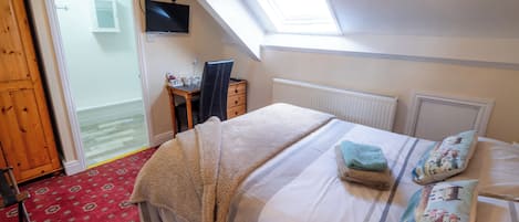A bedroom with a bed, a desk, a chair, a radiator, and a window.