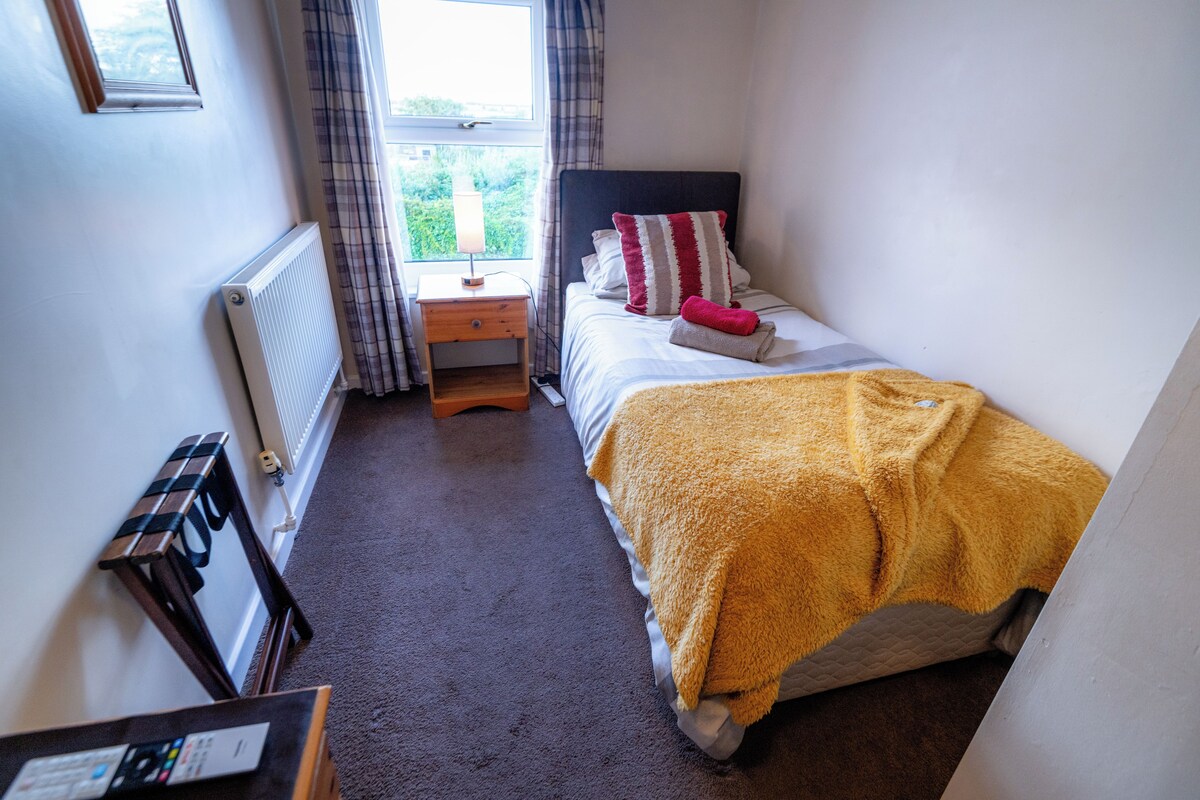 A bedroom with a bed, a nightstand, a window with curtains, and a radiator.