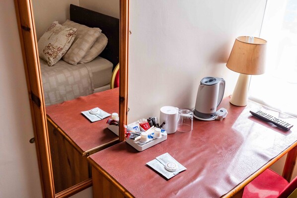 A hotel room with a wooden desk, a lamp, a kettle, a remote control, and a bed with pillows. - Aarondale Guest House (Hartlepool)