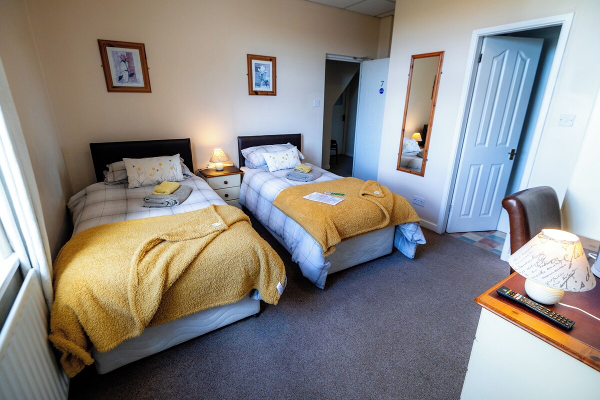 A hotel room with two beds, a desk with a lamp, and a door.