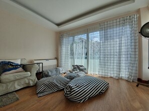 A modern bedroom with a sofa, two striped beds, a radiator, and large windows with patterned curtains.