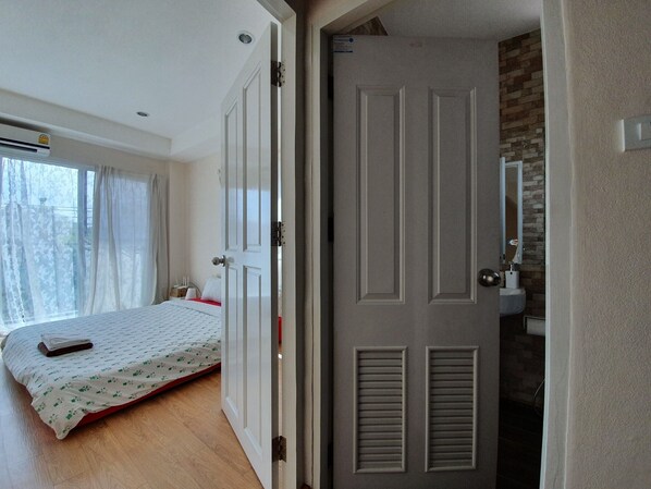 Un dormitorio con cama, ventana con cortinas, aire acondicionado y baño con lavabo y espejo.
