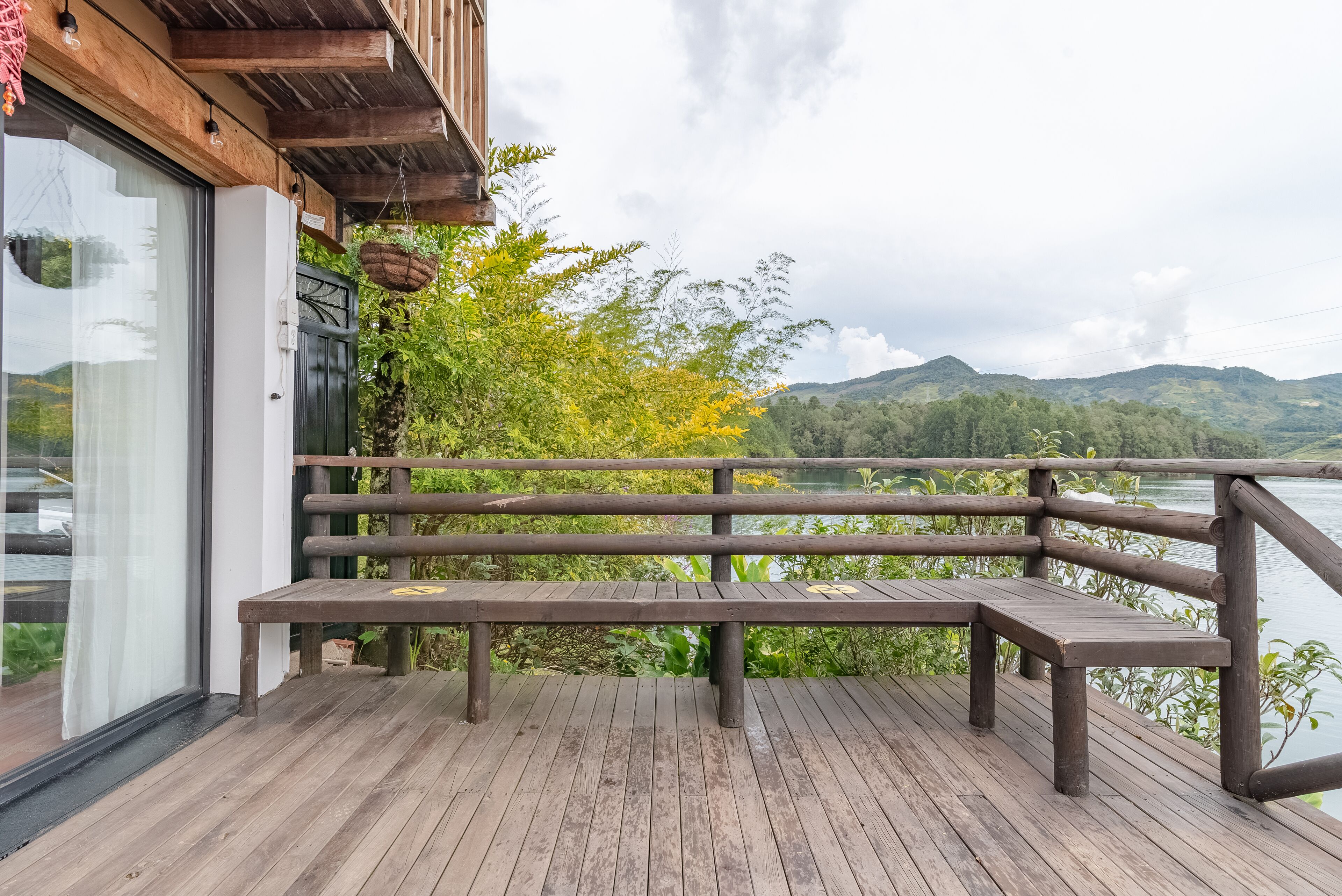 Una terraza de madera con un banco que da a un lago y colinas.