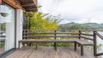 Una terraza de madera con un banco que da a un lago y colinas.