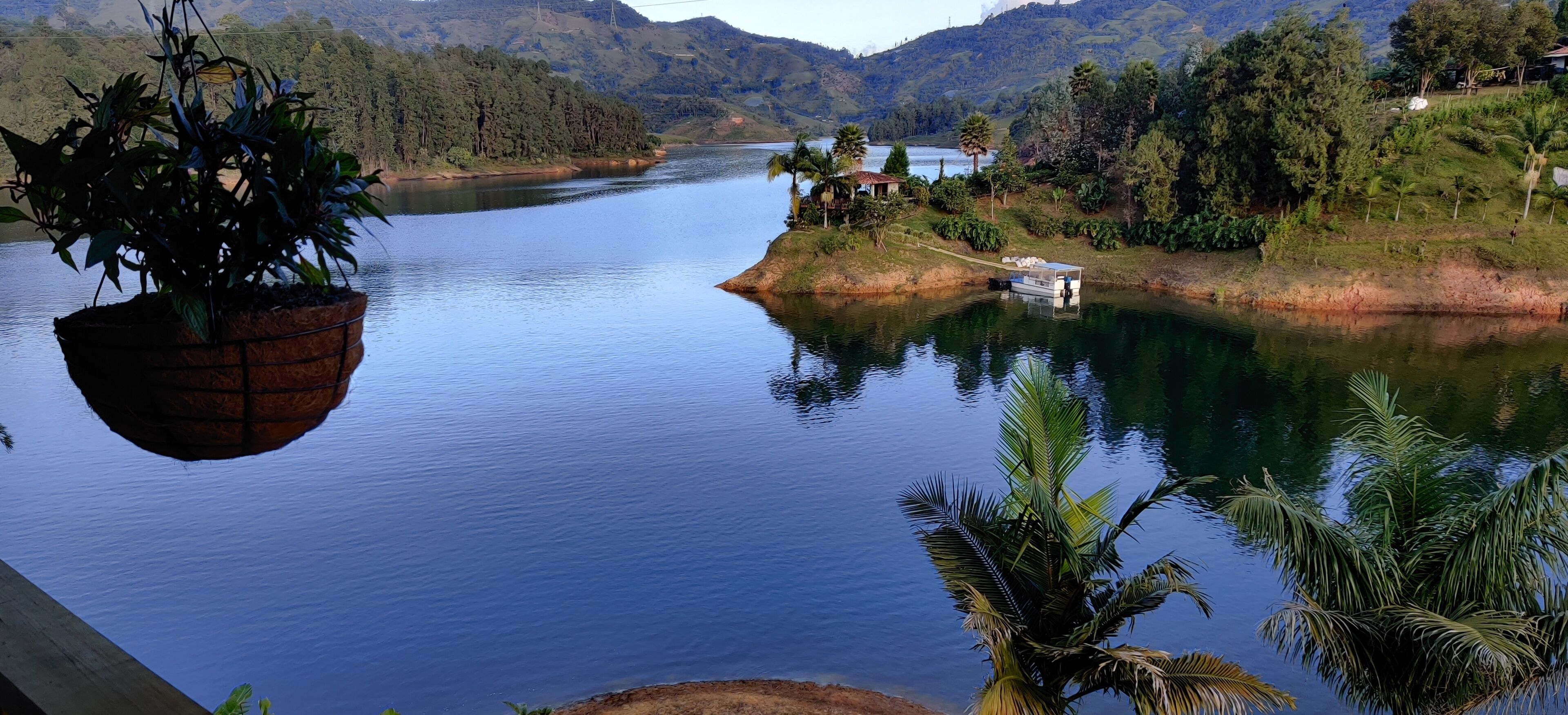 Ein ruhiger See mit einem Boot, das an der rechten Seite anlegt, umgeben von üppiger Vegetation und Hügeln im Hintergrund.