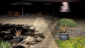 Een houten pad dat naar een strandgedeelte leidt, met ligbedden en een klein gebouwtje.
