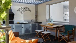 Een overdekt buitenkeuken met een eettafel en stoelen, een raam met uitzicht en een decoratief wandobject.