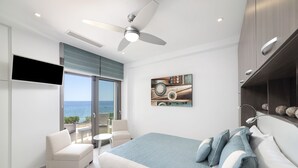 Een moderne slaapkamer met een bed, een plafondventilator, een televisie en uitzicht op zee.
