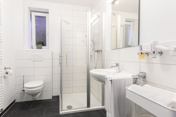 Un baño moderno con cabina de ducha de vidrio, inodoro, lavabo con toalla y espejo.