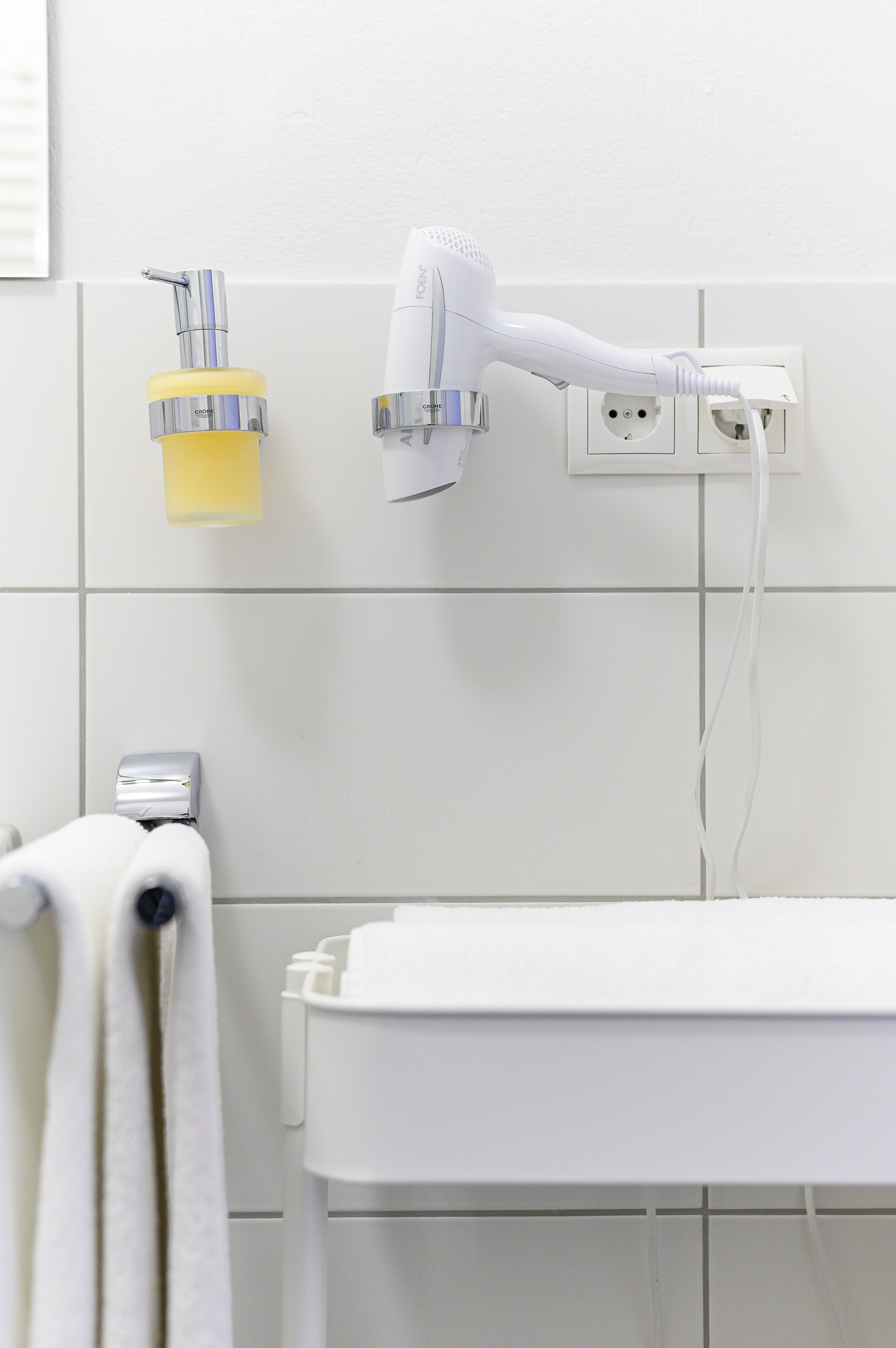 Un baño con un lavabo blanco, un perchero y un secador de pelo conectado a una toma de corriente.