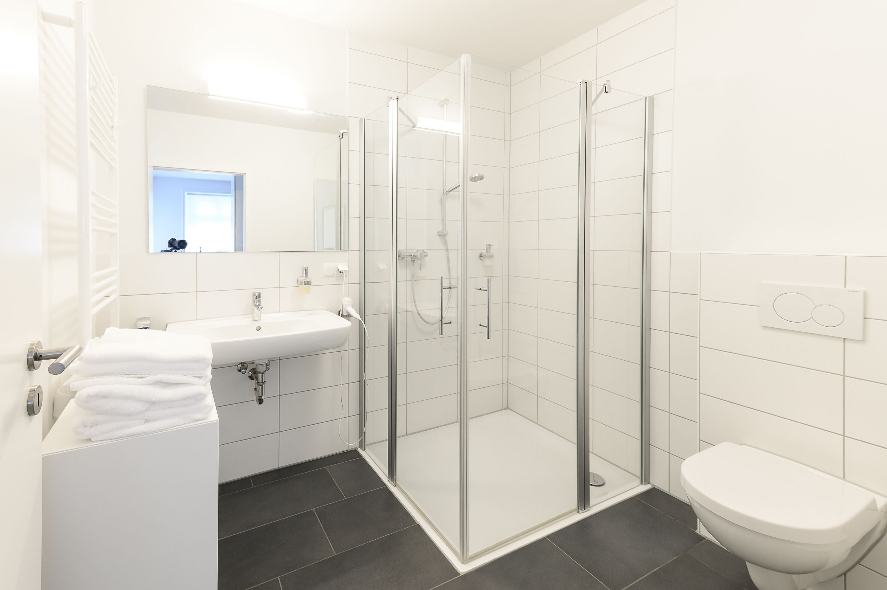 Un baño moderno con ducha envuelta en vidrio, lavamanos blanco con espejo y retrete.
