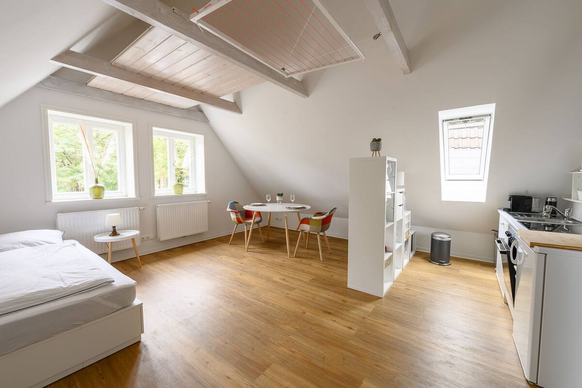 Ein Schlafzimmer mit Bett, einem kleinen Tisch mit Stühlen, einem Fenster und einer Küchenzeile mit Herd und Spüle.