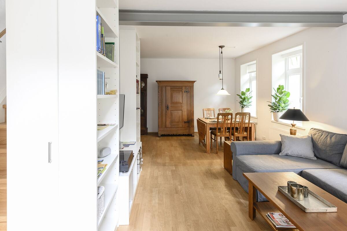 Ein modernes Wohnzimmer mit einer Holztreppe, einem Essbereich und einem Sofa.