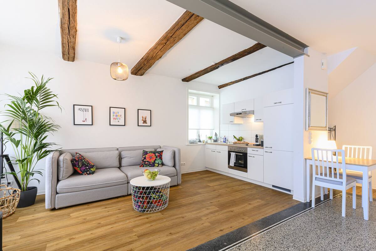 Ein modernes Wohnzimmer mit einem grauen Sofa, einem runden Couchtisch und einem Essbereich mit weißen Stühlen.