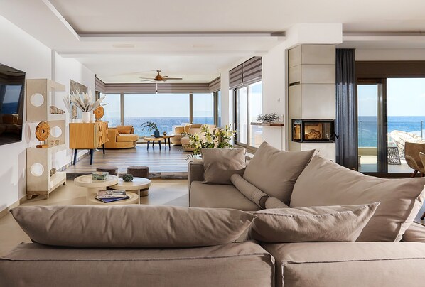 A modern living room with a large beige sofa, a dining area, and a view of the ocean.