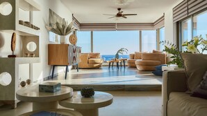 Un salon moderne doté d’une grande fenêtre donnant sur la mer, d’un ventilateur de plafond et d’un décor au style minimaliste.