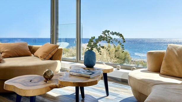 Un salon moderne doté d’une grande fenêtre donnant sur la mer, avec un canapé, une table basse et des objets de décoration.