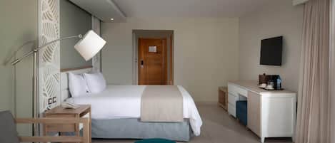 A hotel room with a bed, bedside table, lamp, desk, chair, and a TV mounted on the wall.