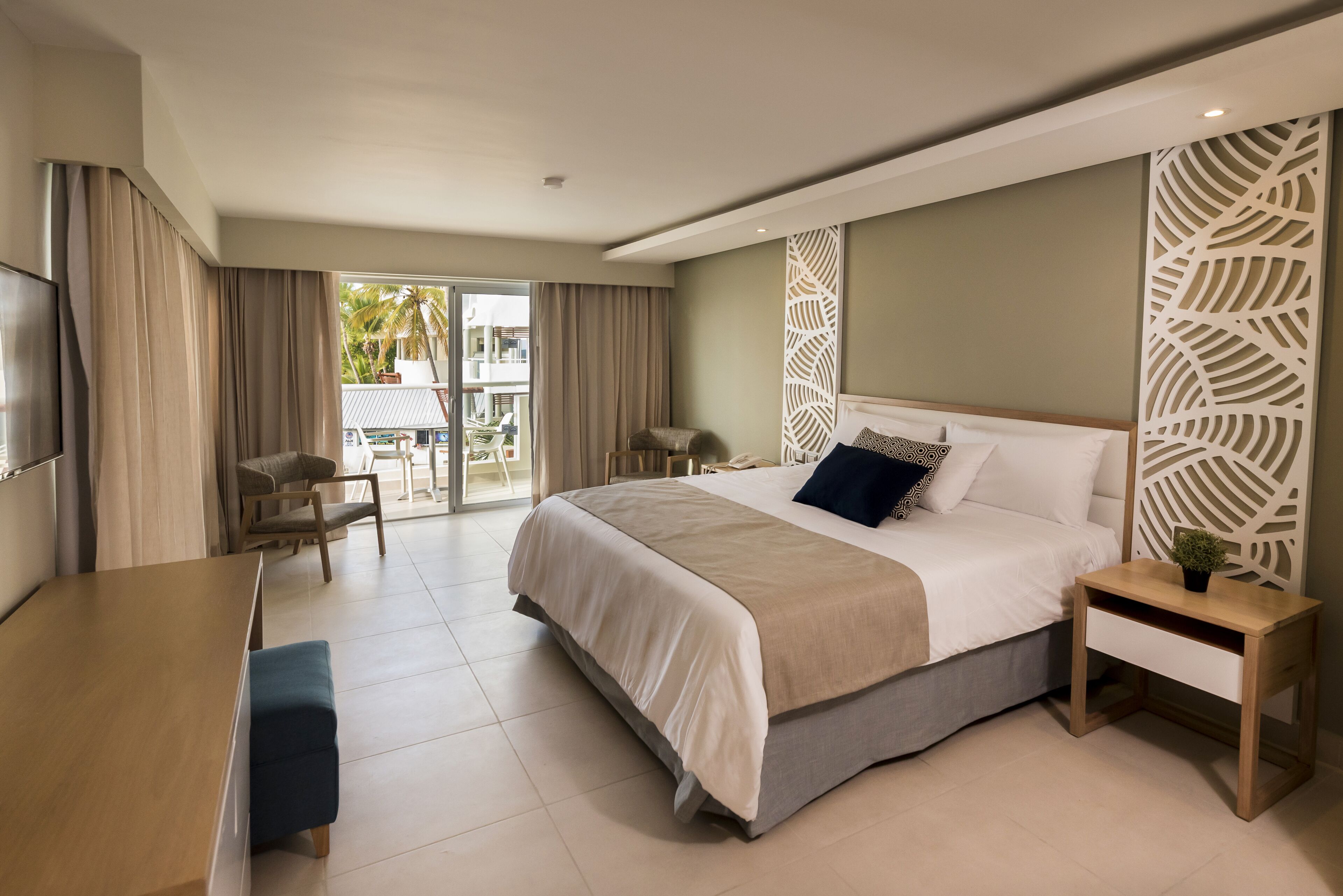 A modern hotel room with a large bed, a desk, and a balcony with a view of palm trees.