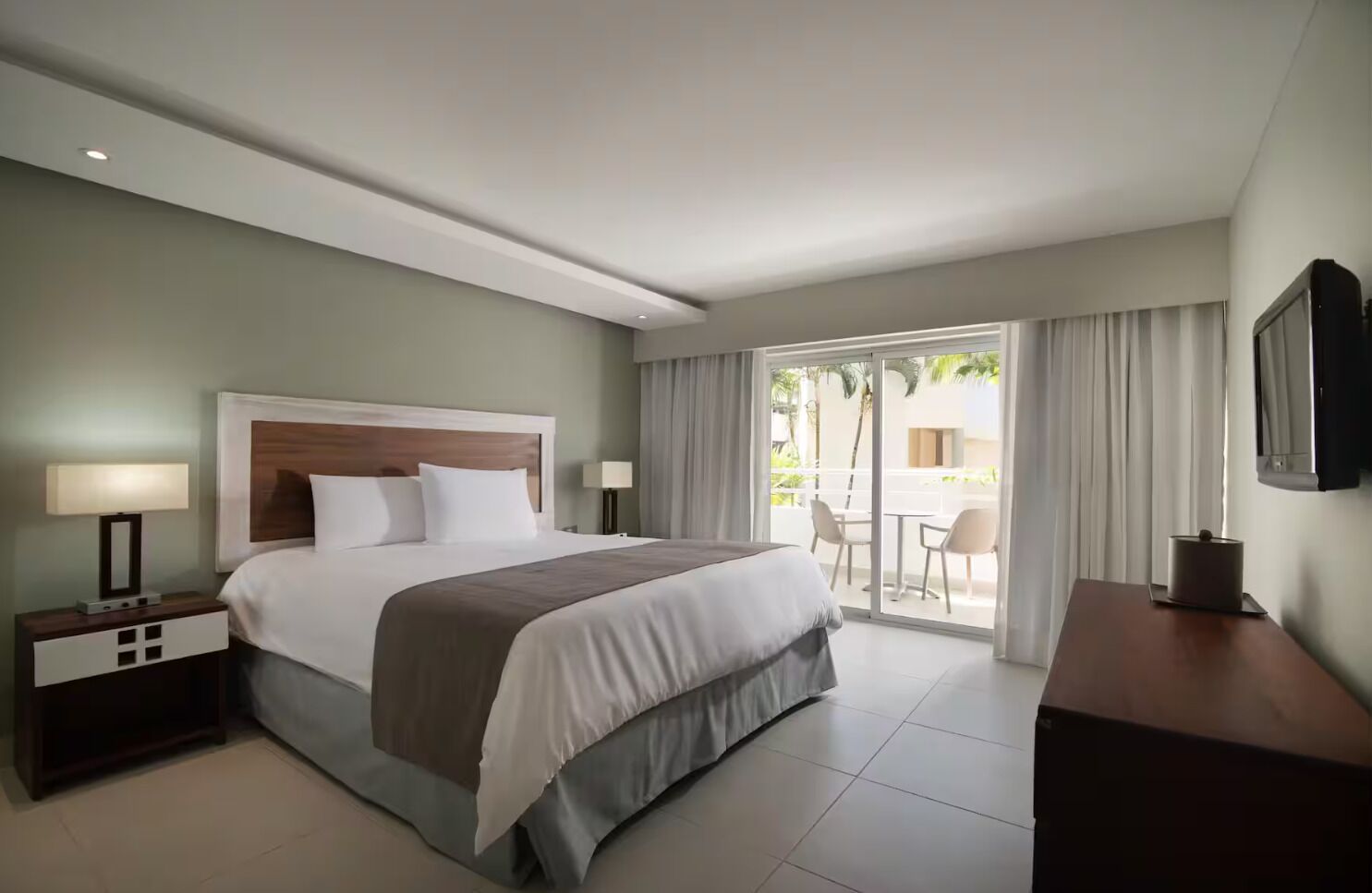 Une chambre d’hôtel comprenant un lit, des tables de chevet, un bureau, une télévision et un balcon avec des sièges d’extérieur.