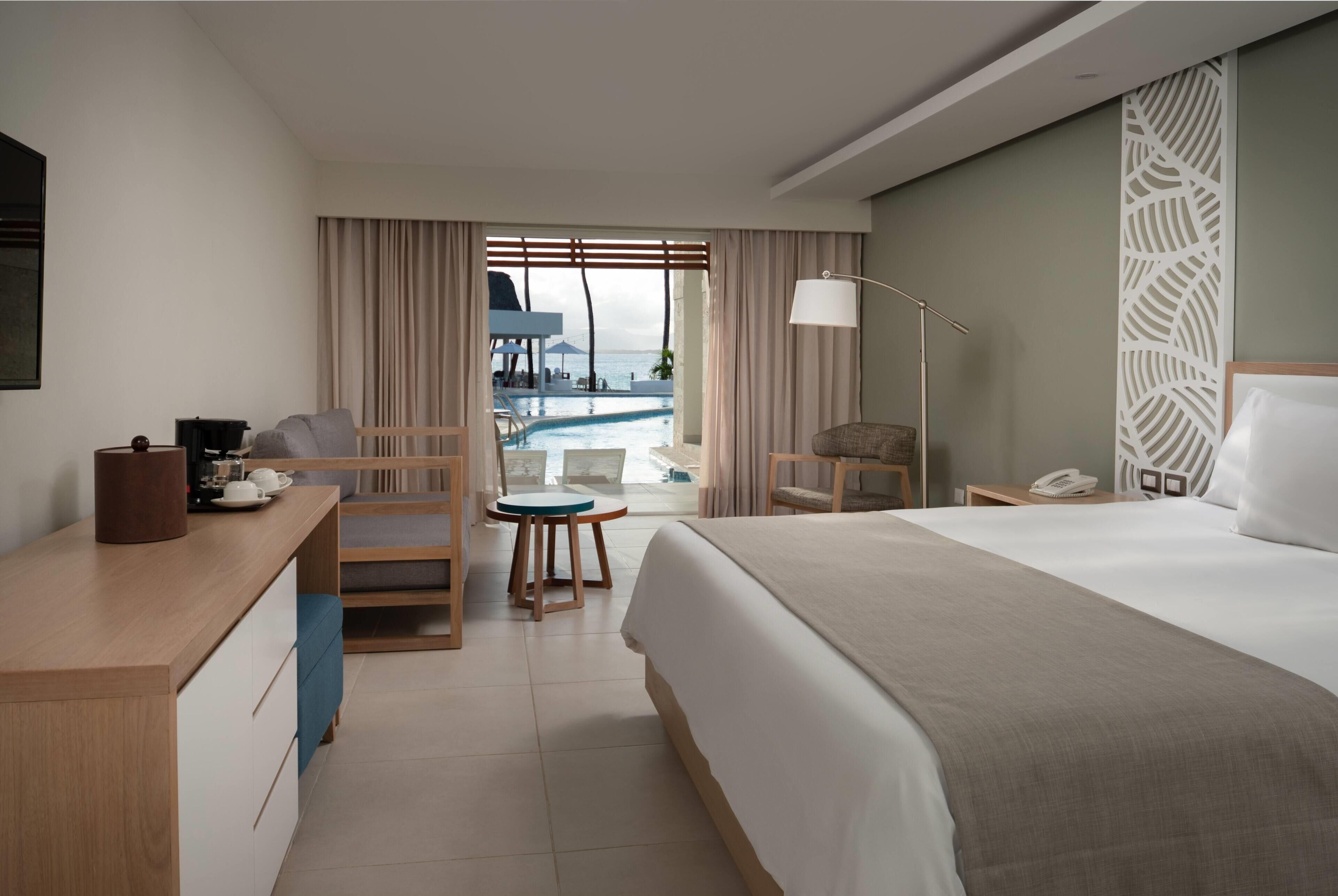 A hotel room with a bed, desk, chair, and a view of a pool.