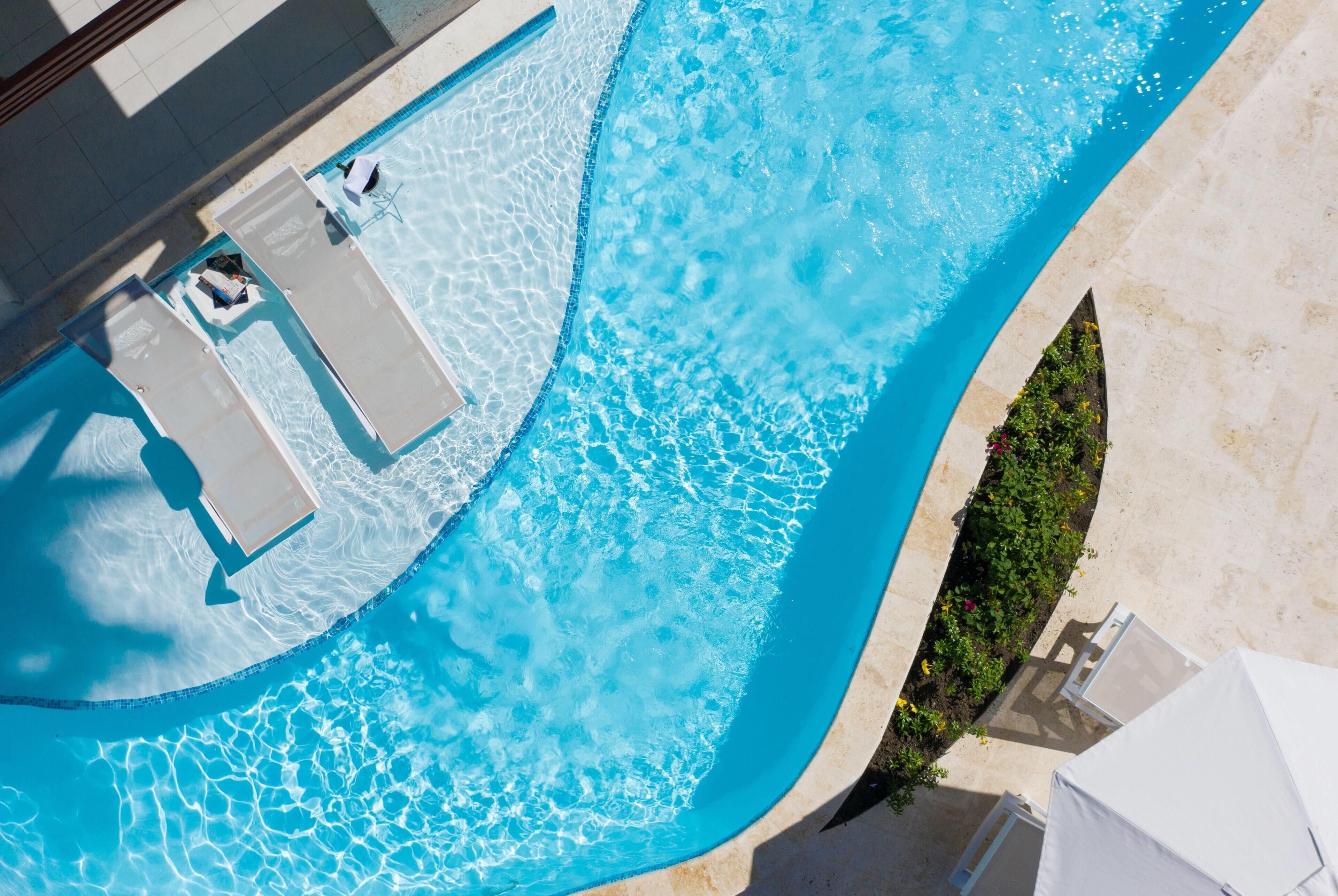 An aerial view of a swimming pool with clear water, surrounded by lounge chairs and a tiled deck.