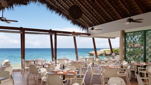 Un restaurante con mesas y sillas dispuestas en una terraza de madera, con vista al océano.