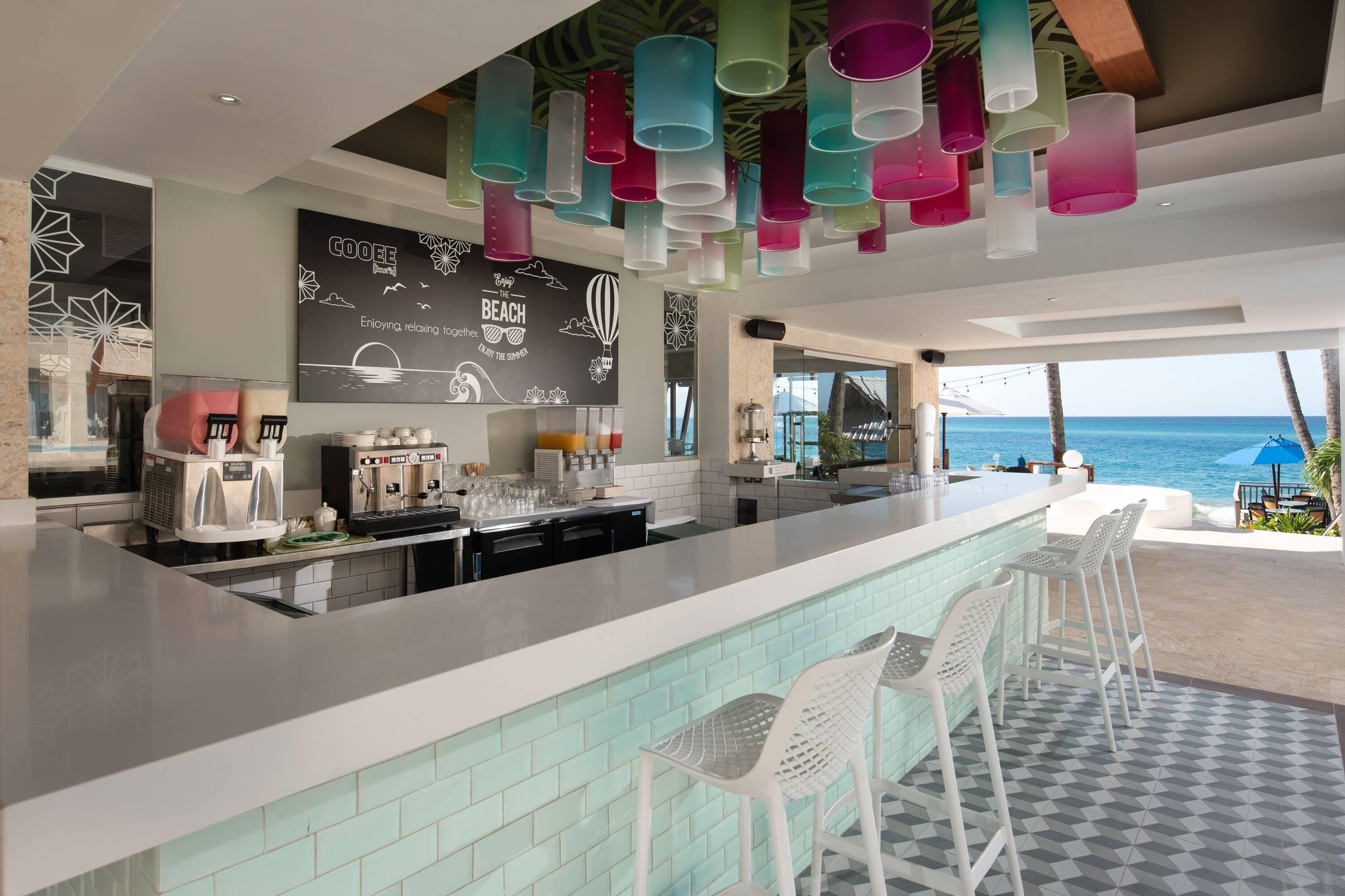 A modern bar area with a long counter, white bar stools, and a view of the ocean.