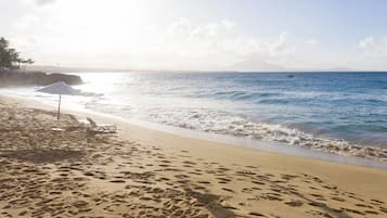 Une plage parsemée d’empreintes, un parasol blanc et un ciel dégagé.