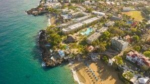 Vista aérea de un complejo turístico costero con alojamiento frente a la playa, piscina y zona de playa.