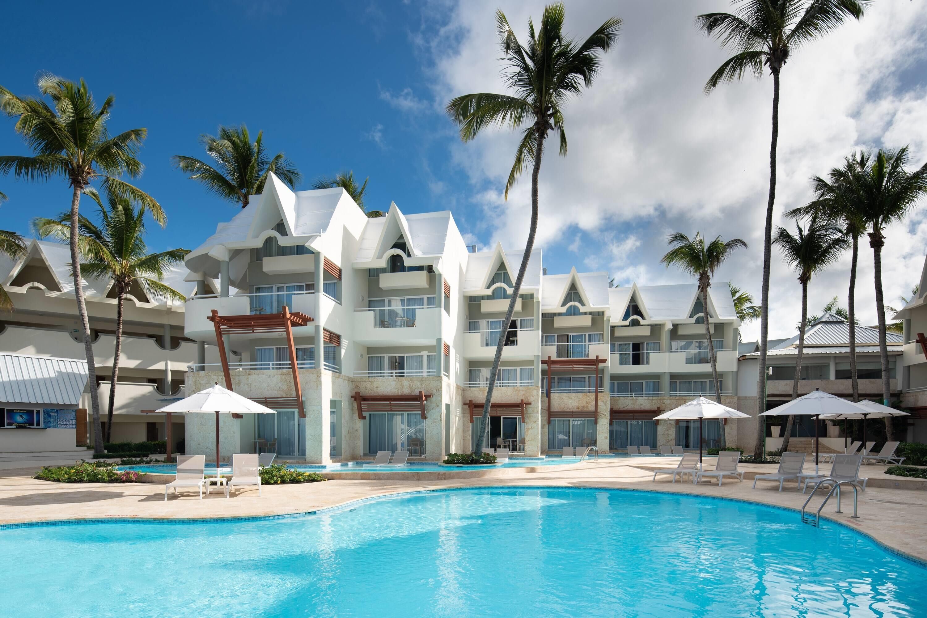 Un resort con piscina, palmeras y un edificio moderno con varios balcones.