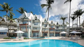 Un resort con piscina, palmeras y un edificio moderno con varios balcones.