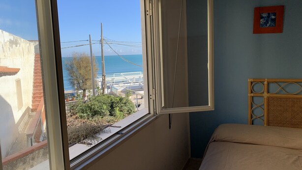 A room with a large window offering a view of the sea and a restaurant. - Hotel Ristorante Il Triangolo (Augusta)