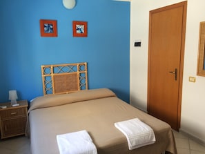 A bedroom with a bed, a nightstand, a wooden door, and two wall-mounted light switches. - Hotel Ristorante Il Triangolo (Augusta)